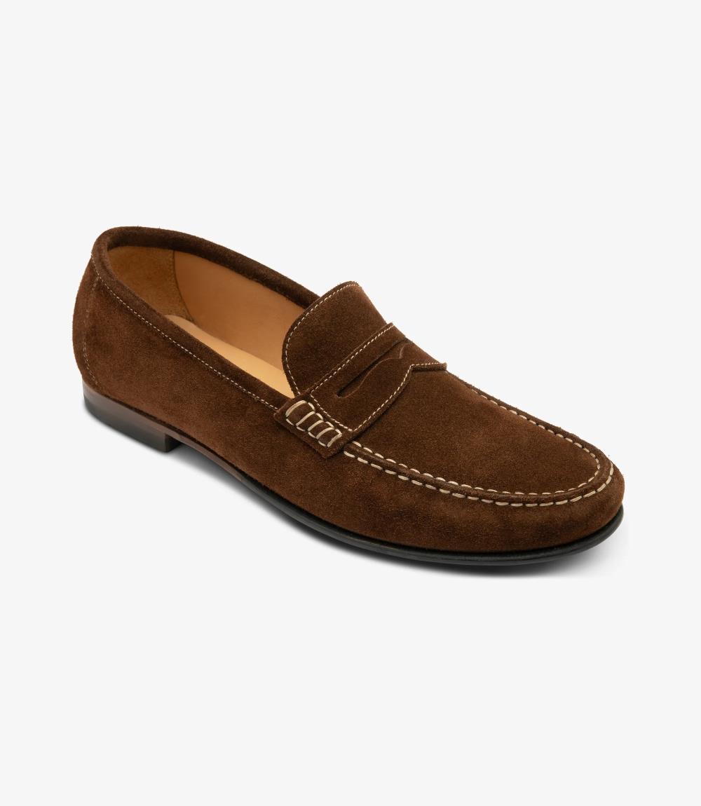 An angled shot highlighting the elegant contours and craftsmanship of the Loake Jefferson Brown Suede Loafer. The supple suede leather gleams under the light, while the moccasin leather/rubber soles provide durability and grip.