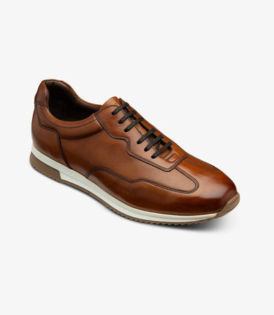 An angled shot capturing the Loake Linford Chestnut Leather Trainer from the side, emphasizing its modern yet timeless aesthetic and the subtle detailing of the design.