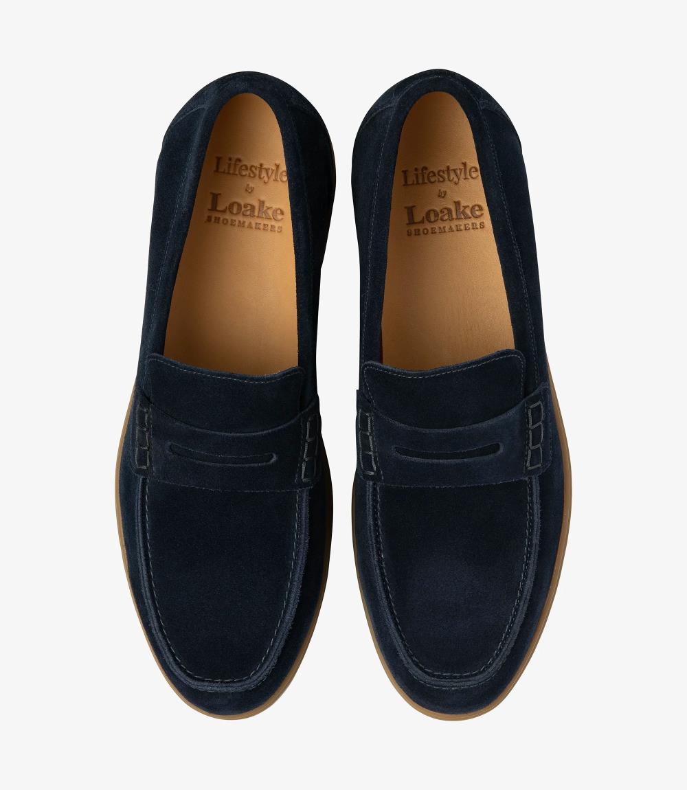 A bird's-eye view presenting a pair of Loake Lucca Navy Suede Loafers, perfectly aligned to showcase their symmetrical design and meticulous craftsmanship. The rich navy suede and fine stitching details are evident from this perspective, epitomizing timeless style and refinement.