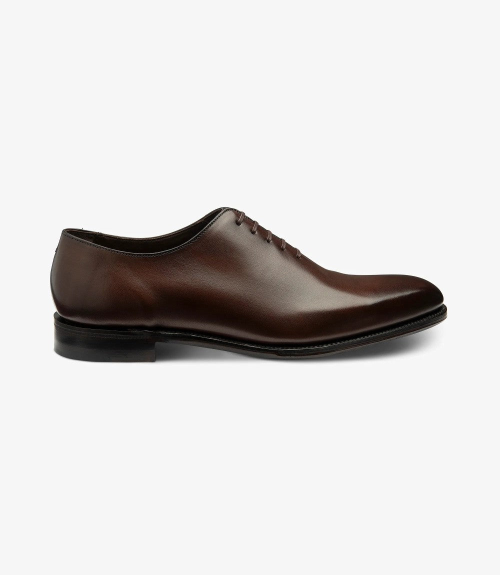 The side view of the Loake Wholebury Dark Brown Oxford Shoes highlights their classic silhouette and elegant lines. The rich dark brown leather upper boasts a polished finish, showcasing the quality craftsmanship that defines the shoe. The Goodyear welt construction is visible where the upper meets the leather sole, emphasizing durability and traditional design.