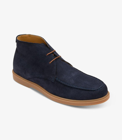 A dynamic angle shot capturing the Loake Amalfi Navy Suede Chukka Boot from the side, highlighting its elegant contours and rounded toe shape. The supple suede leather gleams under the light, while the rubber sole provides stability for every step.