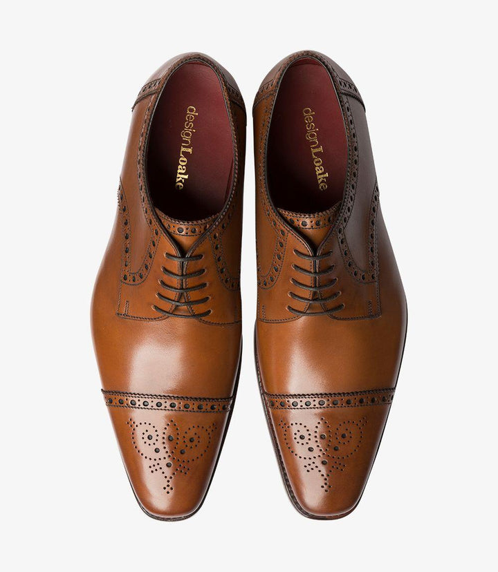 This overhead shot showcases both Loake Foley Cedar Semi Brogues side by side. The symmetry of the shoes highlights their meticulous craftsmanship and attention to detail. The rich cedar leather gleams under the light, while the intricate punched decoration around the toe caps creates visual interest. The Goodyear welted soles are prominently displayed, underscoring the durability and support these shoes offer.