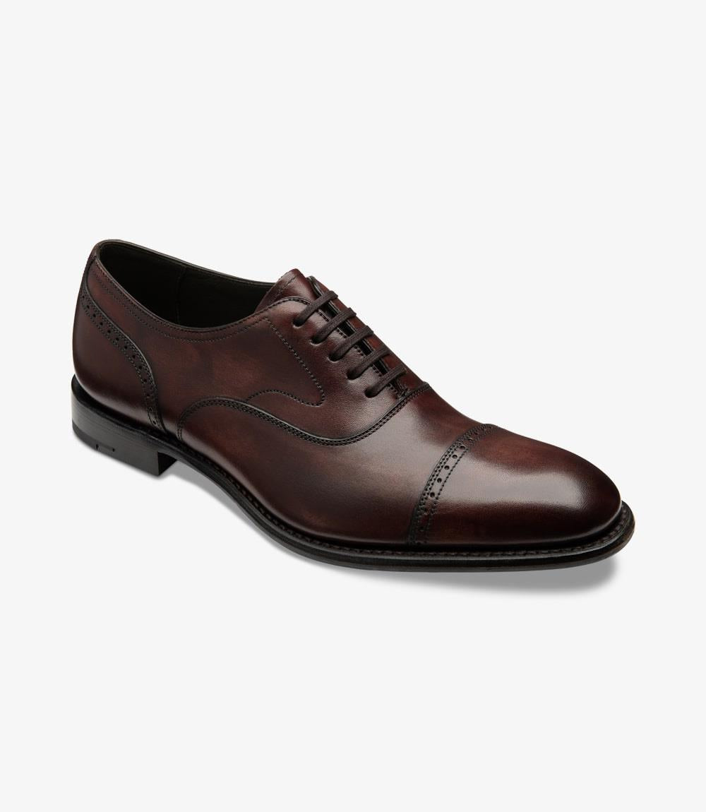 The shoe is presented at a slight angle, allowing a glimpse of both the side and front. This perspective accentuates the intricate brogue detailing around the toe and the smooth curve of the vamp. The rich burgundy hue contrasts beautifully with the leather lining visible through the open space. The shoe's craftsmanship is evident in the fine stitching and the elegant transition from the upper to the sturdy sole, ensuring both style and function.