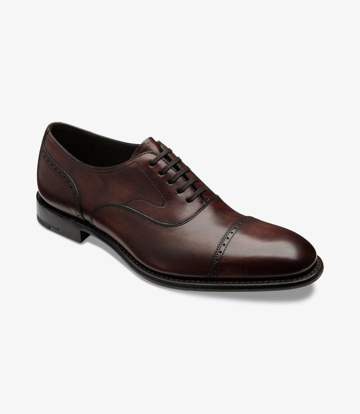 The shoe is presented at a slight angle, allowing a glimpse of both the side and front. This perspective accentuates the intricate brogue detailing around the toe and the smooth curve of the vamp. The rich burgundy hue contrasts beautifully with the leather lining visible through the open space. The shoe's craftsmanship is evident in the fine stitching and the elegant transition from the upper to the sturdy sole, ensuring both style and function.