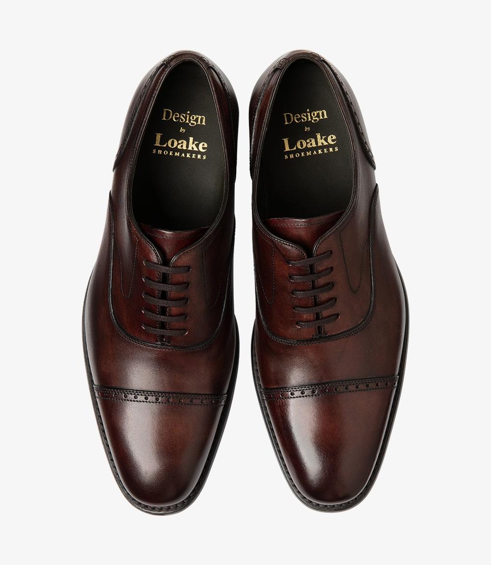 Both shoes are positioned side by side from above, displaying their uniform design and matching burgundy color. The straight toe-caps are neatly aligned, and the punched detailing is visible along the edges. This view captures the overall shape and size, giving a sense of how these semi-brogue shoes will complement a range of outfits. The leather lining peeks out at the opening, hinting at the comfort within.
