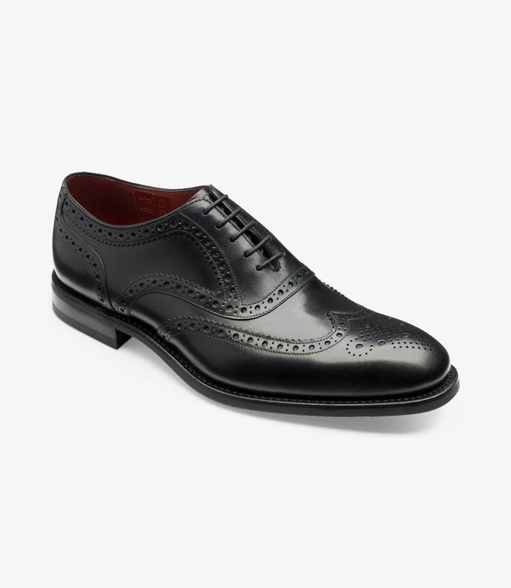 From an angled perspective, the Kerridge Black Oxford exudes sophistication with its polished black leather finish and finely crafted brogue detailing. The intricate spider brogue pattern on the toe and quarters adds a touch of elegance, while the Claridge last shape lends a subtly elongated appearance. The robust rubber sole is partially visible, emphasizing both its durability and style, making it suitable for various occasions.