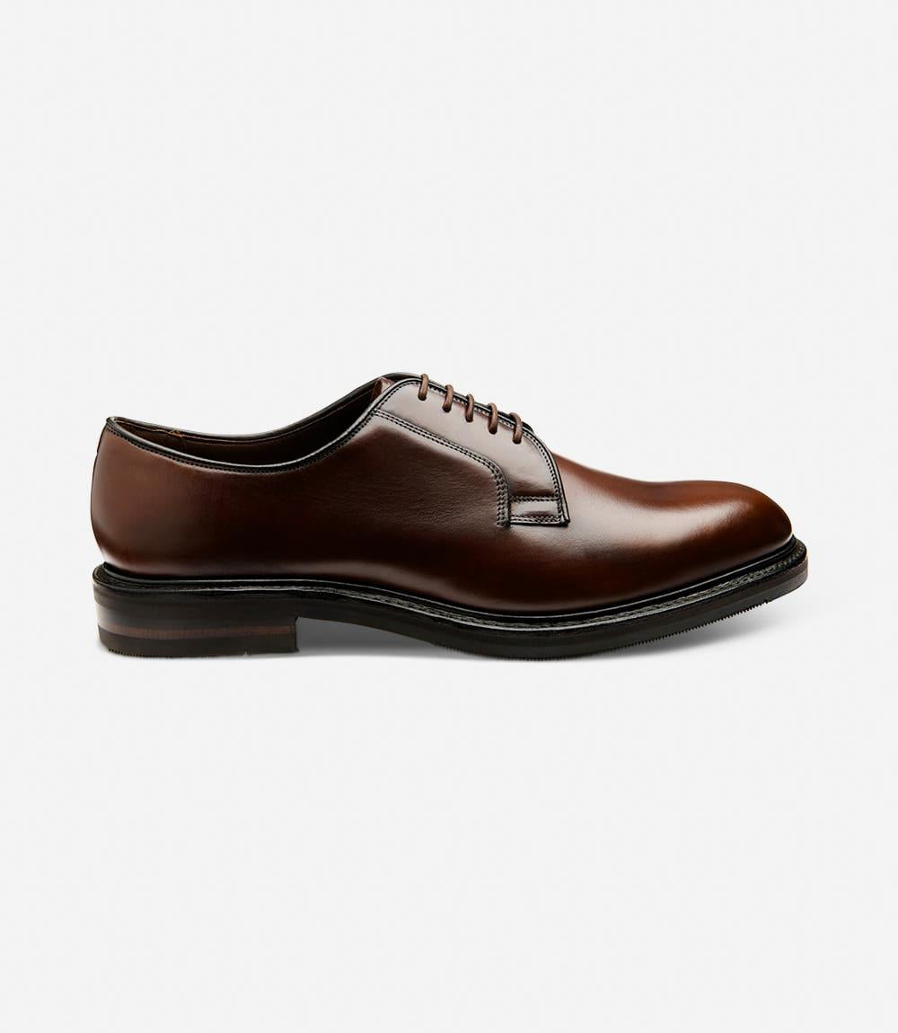 A side view of the Loake Leyburn Dark Brown Derby Toe Cap shoes, showcasing their sleek silhouette and premium hand-painted mahogany grain calf leather upper. The Goodyear welted shadow rubber soles are prominently featured, symbolizing durability and quality craftsmanship.