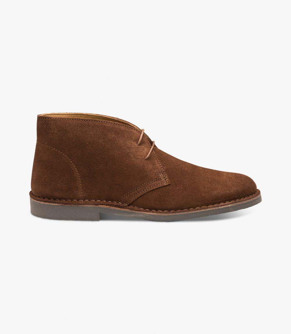 The side view showcases the elegant silhouette of the Sahara Tan Chukka Boot. The premium suede leather upper is rich in color, exuding a warm tan hue that highlights its luxurious texture. The stitched-down rubber sole is clearly visible, emphasizing its durability and the meticulous craftsmanship. The boot's streamlined design features a classic three-eyelet lace-up closure, allowing for an adjustable fit while the gently rounded toe adds a touch of sophistication. The overall profile is clean and refined