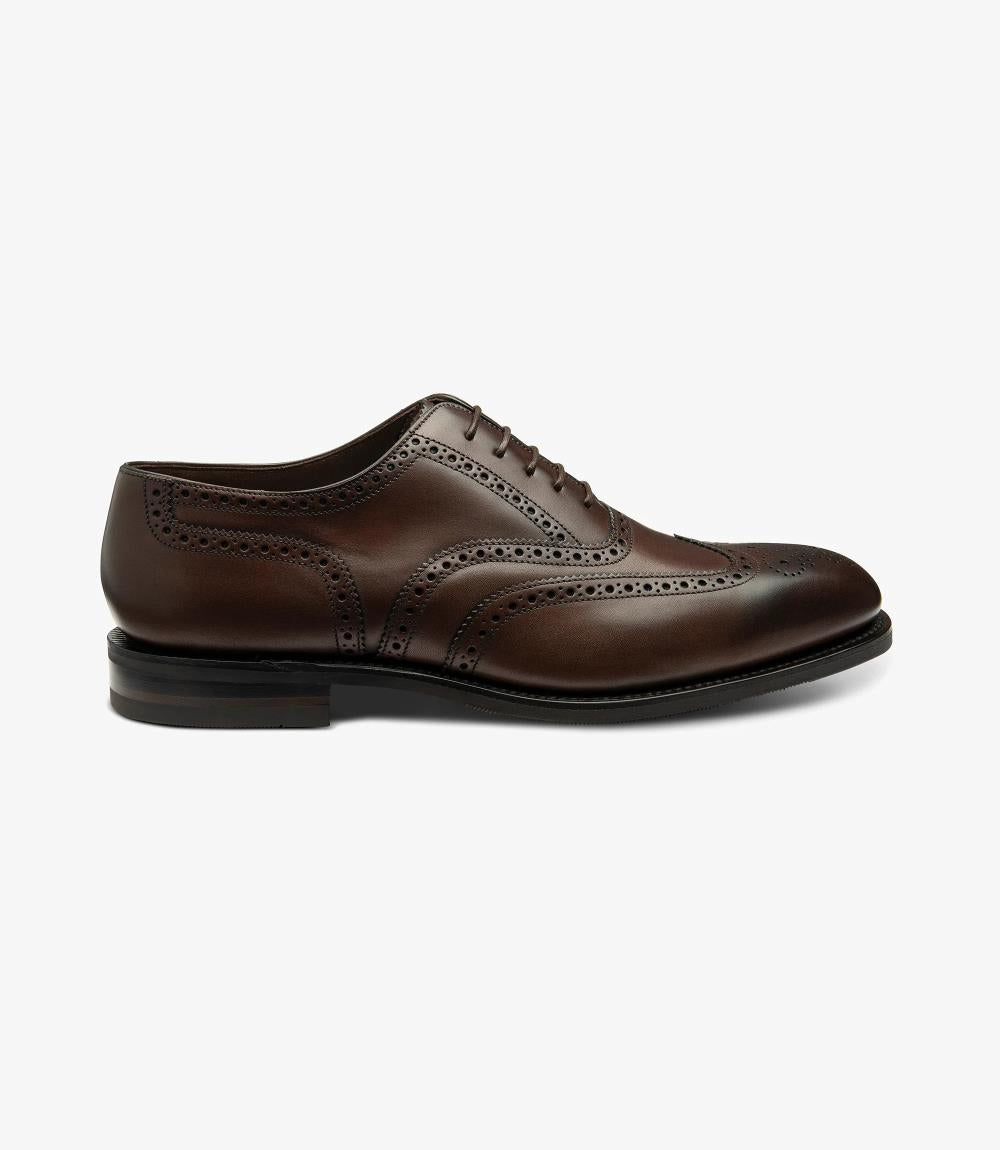 The photo captures a sleek profile of the Loake Buckingham Dark Brown Oxford Brogue. The rich, burnished calf leather glistens under the light, showcasing its elegant texture. The intricate brogue detailing along the edges adds a touch of sophistication, while the Goodyear welted rubber sole provides a sturdy base.