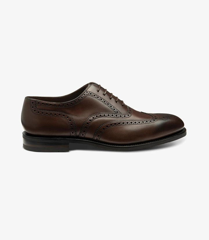 The photo captures a sleek profile of the Loake Buckingham Dark Brown Oxford Brogue. The rich, burnished calf leather glistens under the light, showcasing its elegant texture. The intricate brogue detailing along the edges adds a touch of sophistication, while the Goodyear welted rubber sole provides a sturdy base.