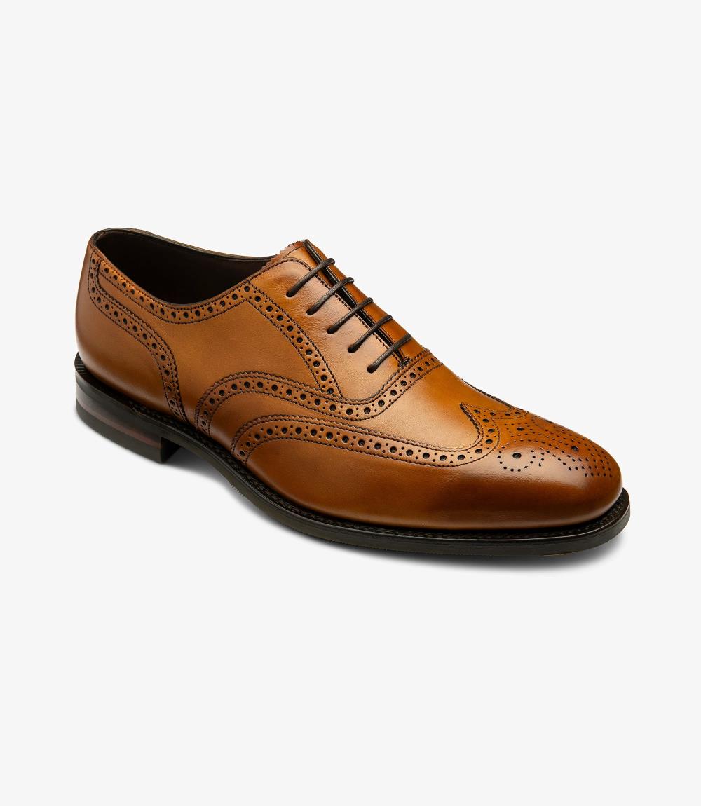 In this angled view, the Loake Buckingham Tan Oxford Brogue reveals its exquisite design features. The combination of the smooth tan leather and detailed broguing creates a sophisticated look that draws the eye. The angled perspective emphasizes the curvature of the shoe, showcasing the leather's rich texture and the elegant stitching that runs along the seams. The sturdy rubber sole is also visible, providing a glimpse of the shoe’s practicality and comfort.