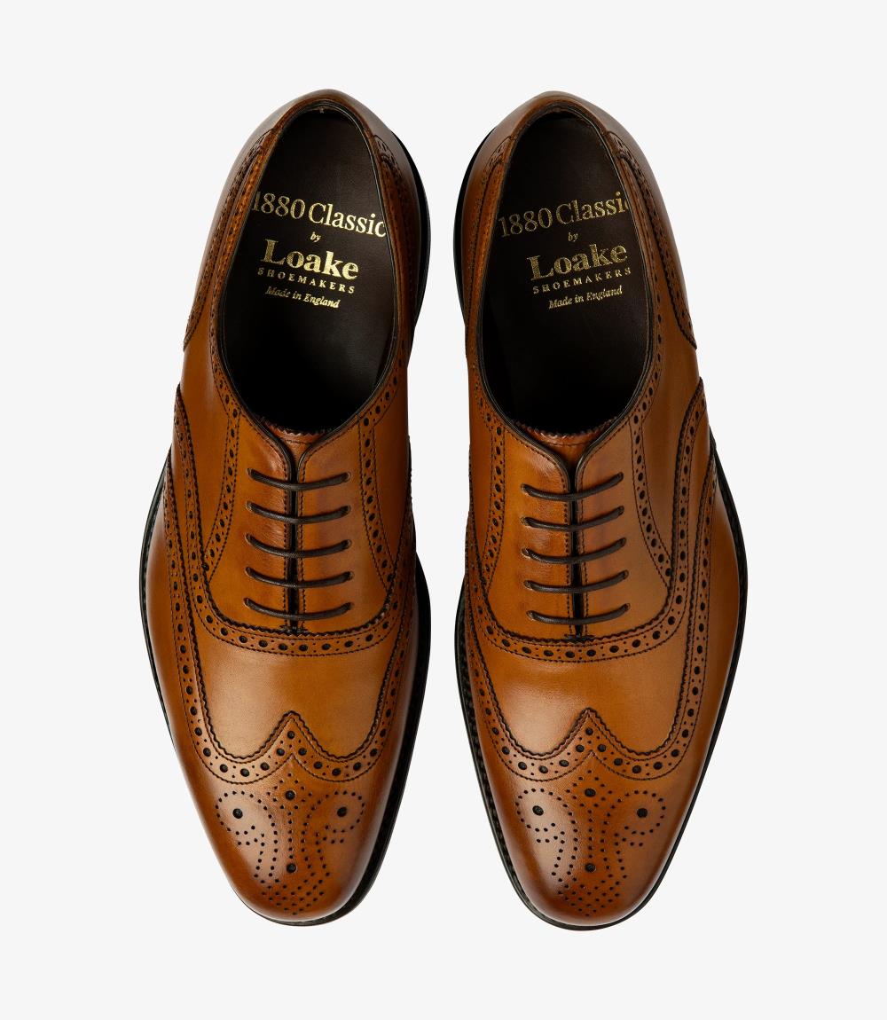 This overhead shot captures both Loake Buckingham Tan Oxford Brogues side by side, emphasizing their symmetry and meticulous craftsmanship. The full brogue design is highlighted, with detailed perforations and elegant stitching clearly visible. The rich tan color of the calf leather is complemented by the polished finish, while the contours of the toe and the slight chisel shape provide a sophisticated aesthetic. The Goodyear welted leather sole can also be seen, showcasing the quality construction.
