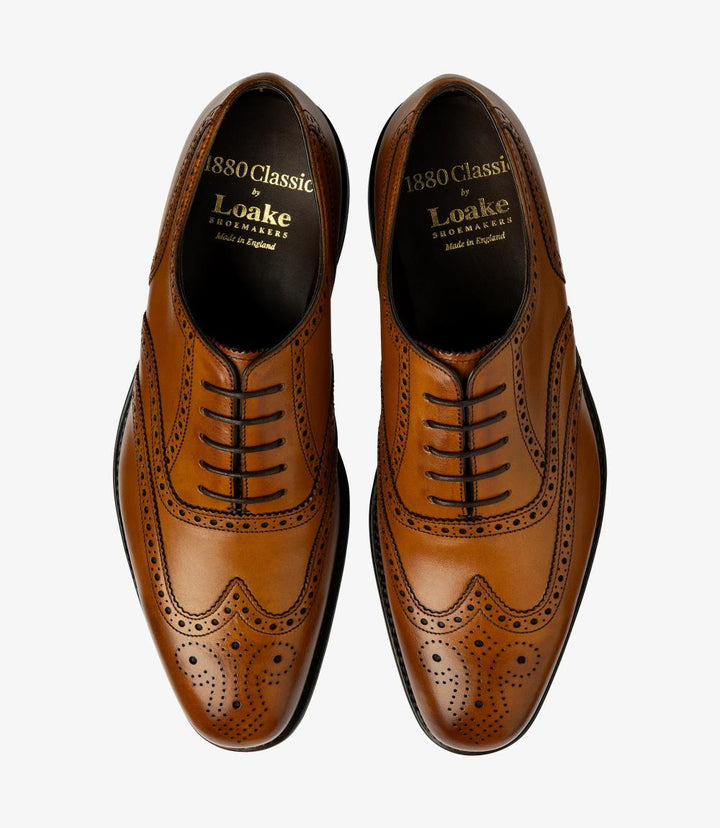 This overhead shot captures both Loake Buckingham Tan Oxford Brogues side by side, emphasizing their symmetry and meticulous craftsmanship. The full brogue design is highlighted, with detailed perforations and elegant stitching clearly visible. The rich tan color of the calf leather is complemented by the polished finish, while the contours of the toe and the slight chisel shape provide a sophisticated aesthetic. The Goodyear welted leather sole can also be seen, showcasing the quality construction.