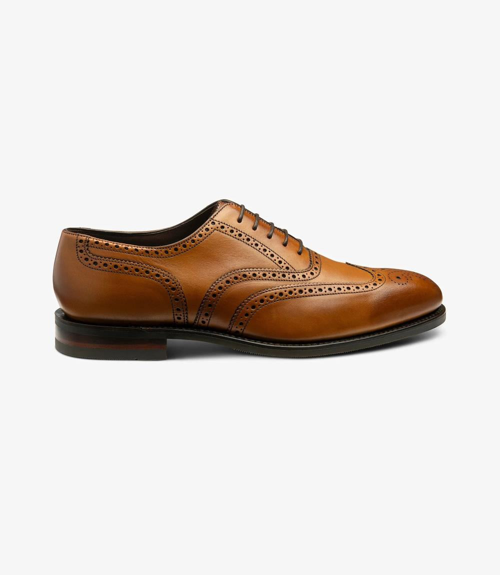 This image showcases the Loake Buckingham Tan Oxford Brogue from a side perspective, highlighting its elegant silhouette. The smooth tan calf leather gleams softly, accentuating the intricate brogue detailing along the toe cap and along the sides. The Goodyear welted construction is evident, demonstrating the shoe's robust craftsmanship. The sleek profile is complemented by the slightly rounded toe and the durable rubber sole, which adds a modern touch to the classic design.