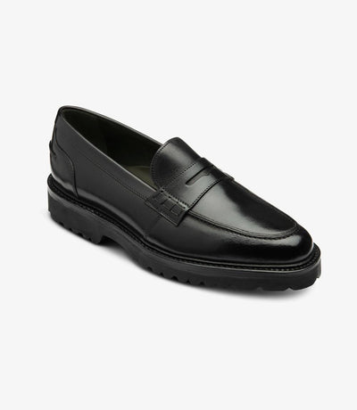 From a dynamic angle, the Loake Crux Black Loafer reveals its modern flair and impeccable craftsmanship. The black calf leather gleams under the light, while the commando sole adds durability and grip. The sleek profile of the shoe highlights its versatility and sophistication.