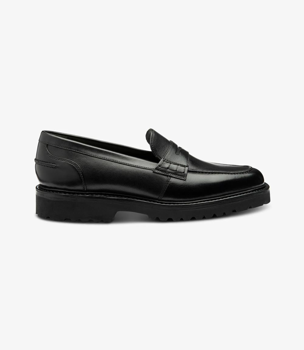 A sleek silhouette of the Loake Crux Black Loafer showcases its premium calf leather construction and contemporary design. The commando sole adds a rugged yet stylish touch, perfect for versatile wear.