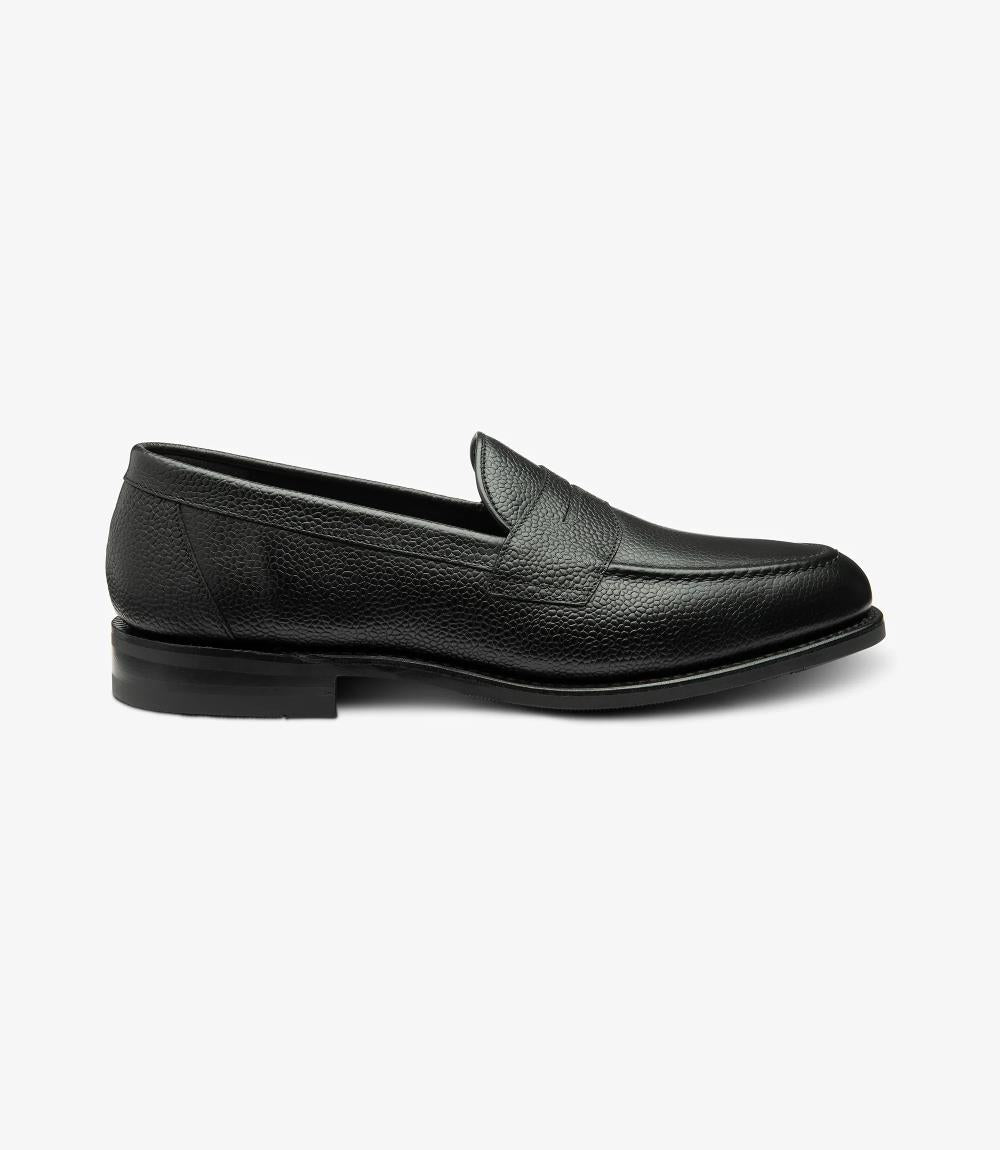 The side view of the Imperial Grain Black Loafer highlights its sleek and elegant design, showcasing the rich texture of the grain calf leather. The polished surface glistens under the light, accentuating the deep black hue. The classic apron design features meticulous stitching that adds sophistication, while the Goodyear welted shadow rubber sole emphasizes durability and quality. 