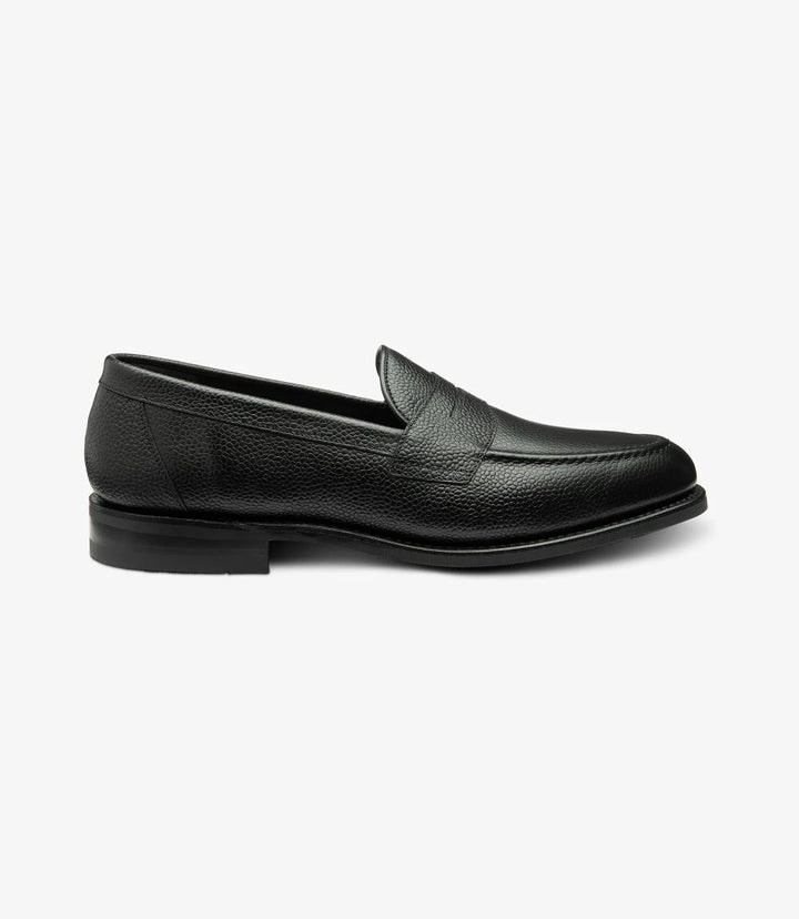 The side view of the Imperial Grain Black Loafer highlights its sleek and elegant design, showcasing the rich texture of the grain calf leather. The polished surface glistens under the light, accentuating the deep black hue. The classic apron design features meticulous stitching that adds sophistication, while the Goodyear welted shadow rubber sole emphasizes durability and quality. 