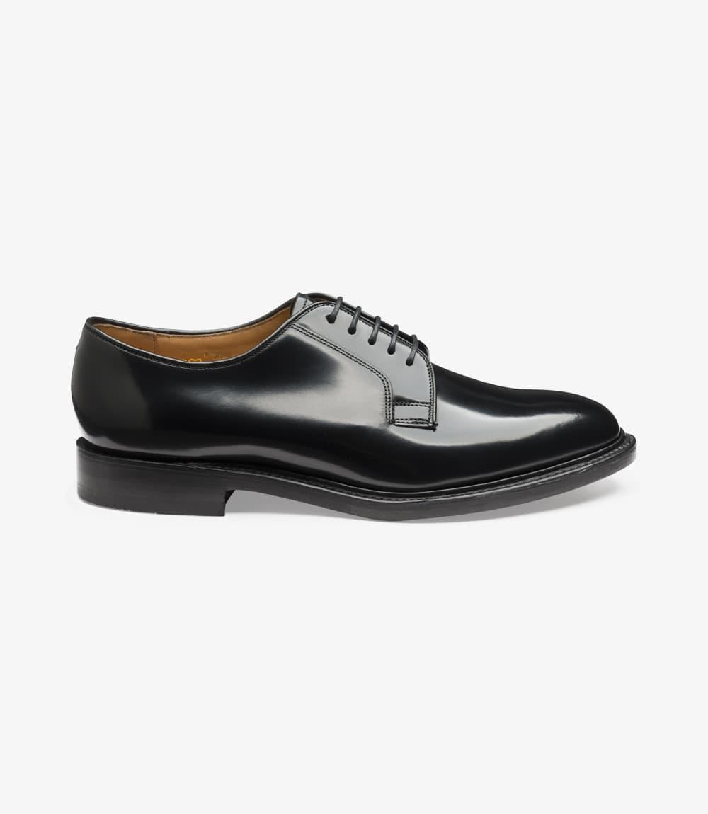 A close-up view shows the Loake 771 Black Derby shoe from the side, highlighting the polished black leather upper with its smooth, classic plain front. The clean silhouette and well-defined Goodyear welt along the double leather sole emphasize the shoe's high-quality construction and durability.