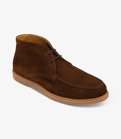 A dynamic angle shot capturing the Loake Amalfi Chocolate Suede Chukka Boot from the side, highlighting its elegant contours and rounded toe shape. The supple suede leather gleams under the light, while the rubber sole provides a sturdy foundation for every step.