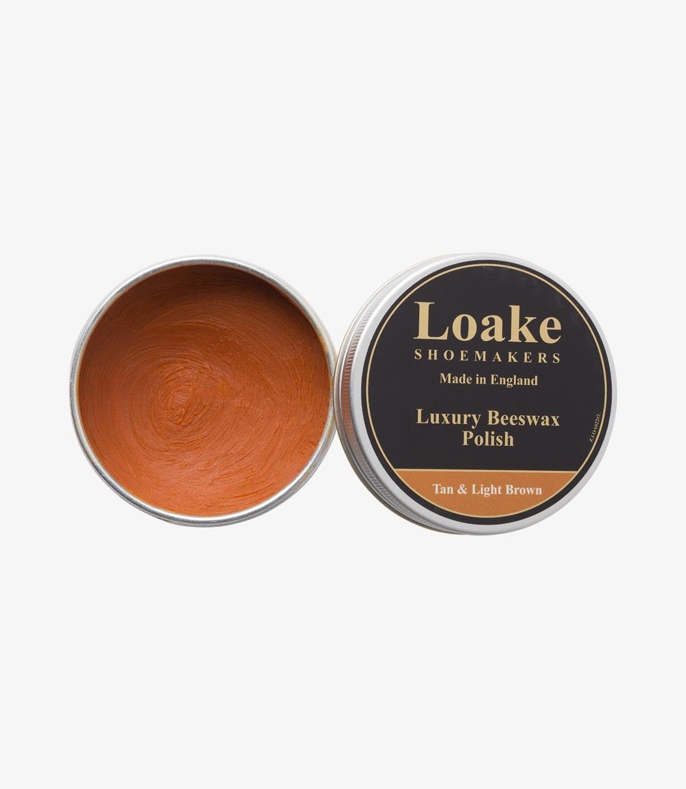 The Loake Saphir Cream Polish in Mahogany showcases a sleek and elegant design. The glass jar features a gold label with black text, clearly displaying the product name and its mahogany color. The creamy polish inside glistens slightly under the light, suggesting its rich texture. The lid is a shiny black, adding a touch of sophistication to the overall look of the product. The polish sits on a clean, neutral surface, emphasizing its premium quality.