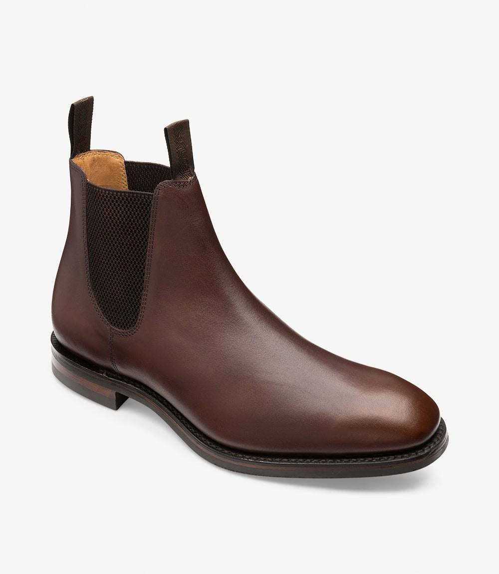 Captured from an angle, this image presents the Loake Chatsworth Chelsea Boot, revealing its sleek lines and the curvature of the heel. The waxed suede leather appears soft yet durable, and the contrasting Dainite rubber sole adds a modern touch to the traditional design. The boot's generous 'G' fitting can be observed, offering a comfortable fit while enhancing its overall refined look.