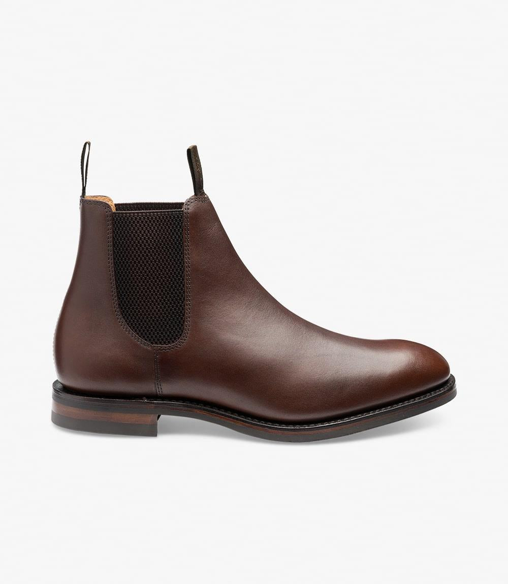 This photo showcases the side profile of the Loake Chatsworth Dark Brown Leather Chelsea Boot. The waxed leather upper gleams with a rich, dark brown finish, highlighting its smooth texture. The elegant, streamlined silhouette is complemented by elastic side panels, ensuring easy wear while maintaining a classic aesthetic. The Goodyear welt construction is subtly visible, emphasizing the boot's quality craftsmanship.