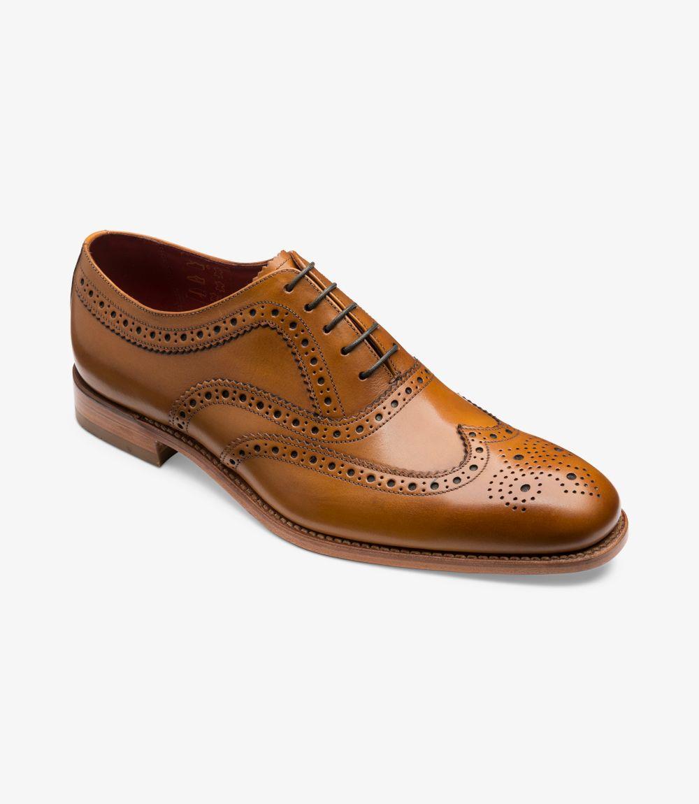 In this angled view, the shoe's distinct features come to life. The combination of the rich tan leather and the brogue detailing creates a striking contrast, drawing attention to the intricate craftsmanship. The curvature of the shoe is beautifully highlighted, with the leather gently reflecting light. This perspective also emphasizes the comfortable fit provided by the Claridge last shape, showcasing how it gracefully contours to the foot while maintaining a sharp, polished look.