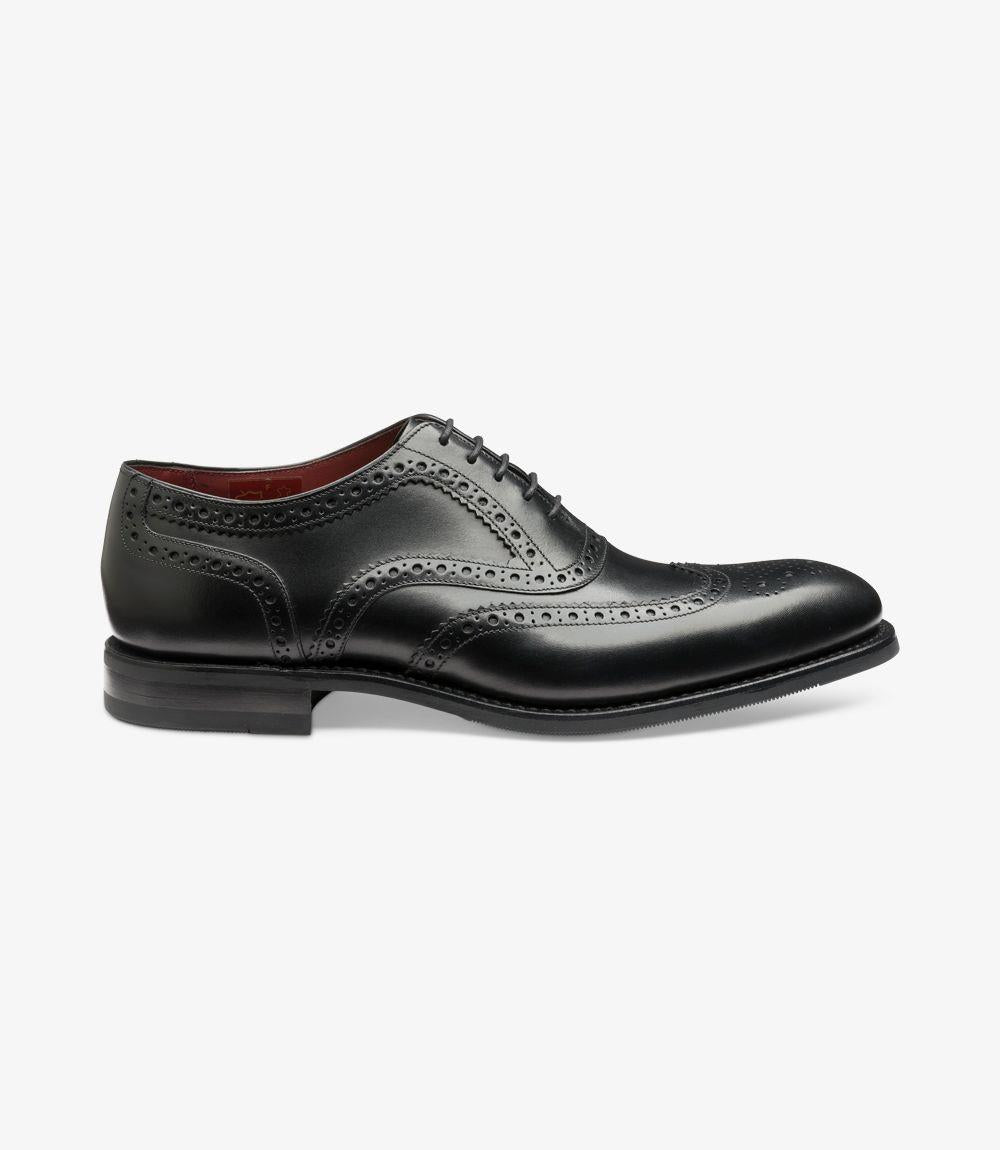 The Loake Kerridge Black Oxford showcases a sleek profile, featuring smooth, hand-painted black calf leather with intricate punched brogue detailing along the seams and toe cap. The shoe's elegant silhouette is complemented by a slightly rounded toe and a low stacked heel. The durable Goodyear welted 'Shadow' rubber sole provides stability and a classic touch, while meticulous stitching enhances the overall refined look.