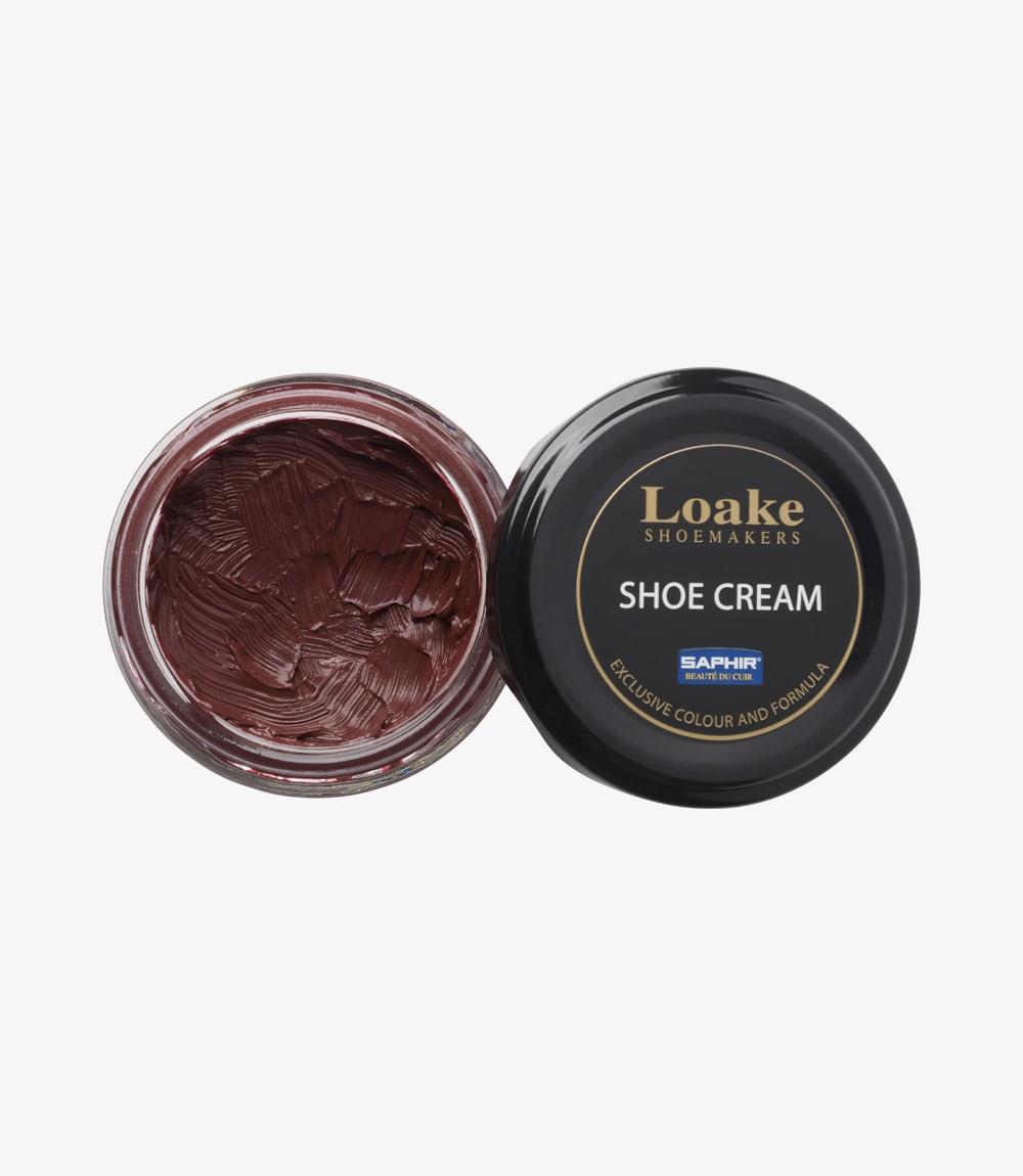 The image shows the side of the Loake Saphir Cream Polish container, revealing its elegant design. The mahogany cream polish is housed in a compact, cylindrical glass jar with a shiny black lid. The label on the front features the Loake logo prominently displayed, along with details about the cream's purpose and colour.