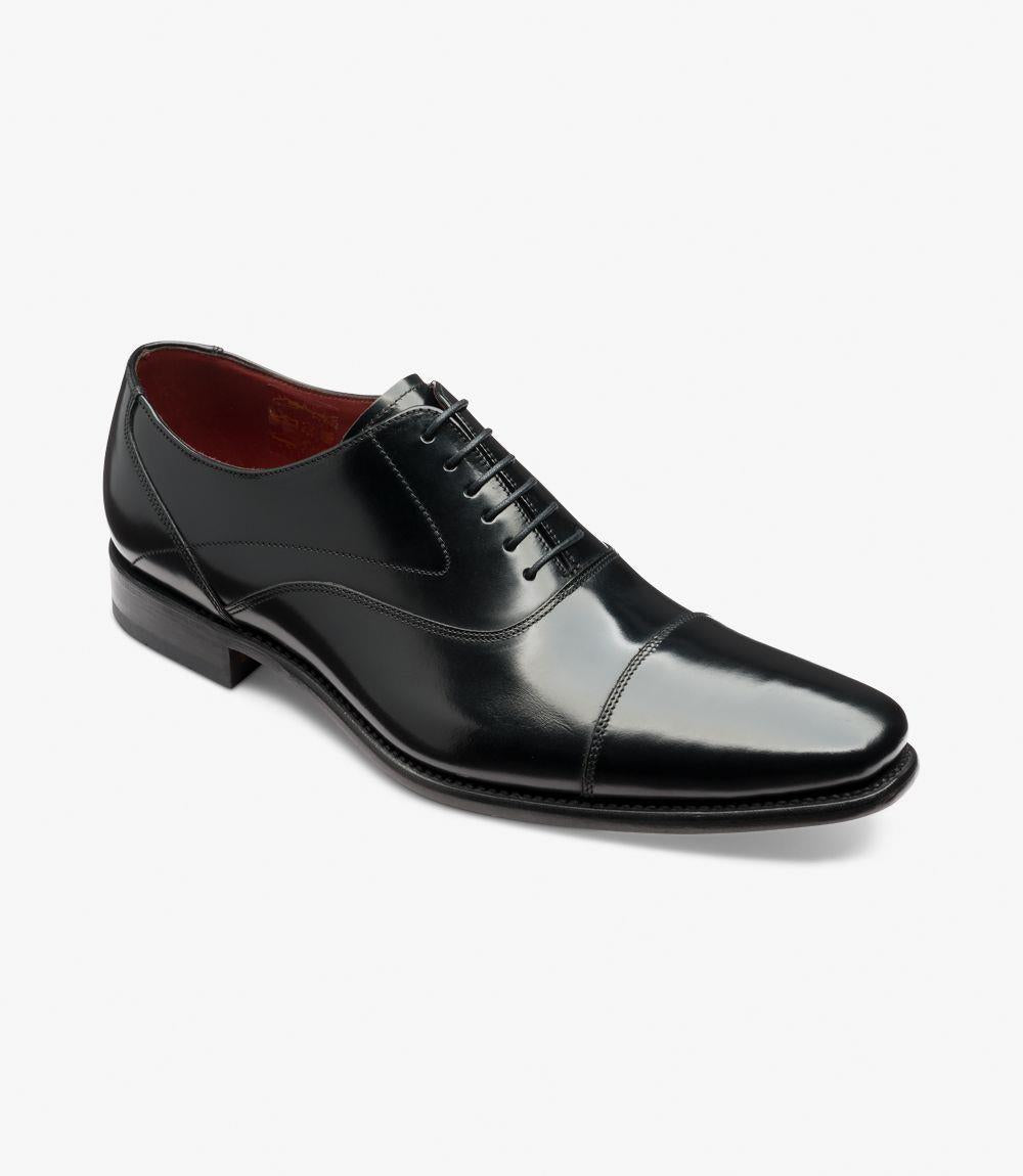 The angle view of the Loake Sharp Black Oxford captures the shoe’s refined profile and meticulous craftsmanship. From this perspective, the toe-cap detail is prominent, highlighting the polished finish and smooth lines of the leather. The curvature of the upper and the structured heel give a sense of support and style, while the side-stitching along the rubber sole is visible, showcasing the shoe's quality construction and attention to detail.