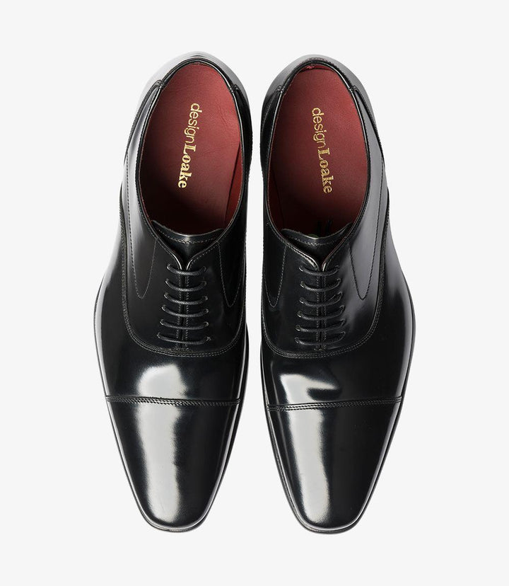 The top-down view of the Loake Sharp Black Oxford offers a comprehensive look at its classic design. The clean lines of the upper are accentuated by the symmetrical arrangement of the eyelets and laces, which are neatly threaded through the reinforced openings. The toe-cap detail is clearly visible, enhancing the shoe's sophisticated appearance. This view highlights the overall elegance and polished finish that make this Oxford a timeless choice for formal wear.