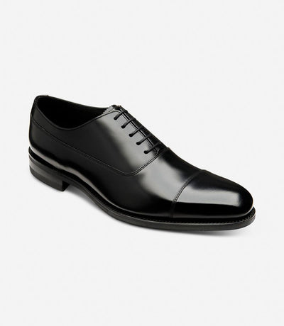 From a dynamic angle, the Loake Truman Black Polished Oxford reveals its meticulous craftsmanship and attention to detail. The polished black leather gleams under the light, exuding sophistication and elegance. The sleek profile of the shoe highlights its timeless appeal and versatility.